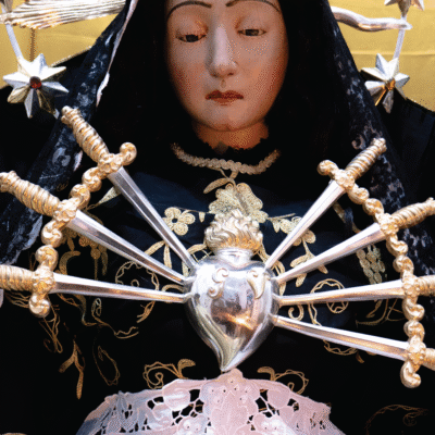 Sul manifesto il volto della Madonna Addolorata scultura lignea settecentesca custodita nella Chiesa Arcipretale di Santa Barbara in Taverna (CZ).